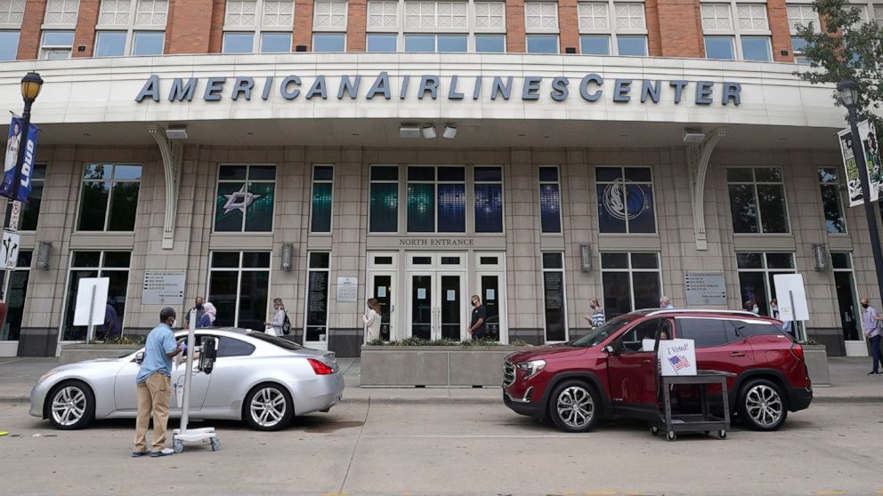 Voters cast their ballot from their vehicles as others line up and wait outside the American Airlines Center during early voting for the general election Thursday, Oct. 15, 2020, in Dallas. (AP Photo/LM Otero)