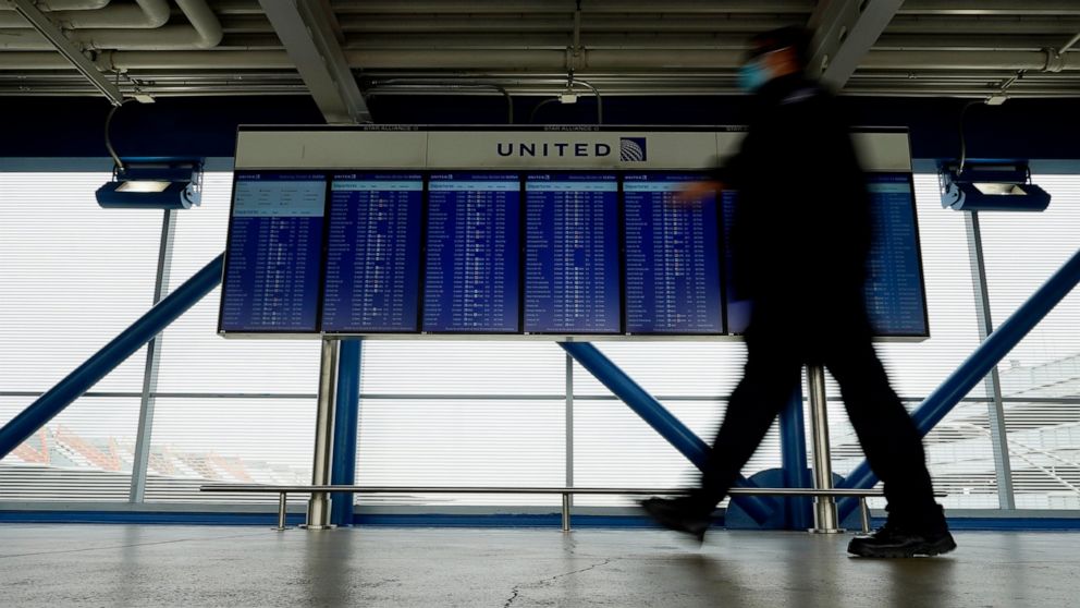 FILE - In this Oct. 14, 2020 file photo, a TSA staff wears mask as he walks past flight information screens show flight status information at O'Hare International Airport in Chicago. Federal officials keep seeing cases of airline passengers getting i