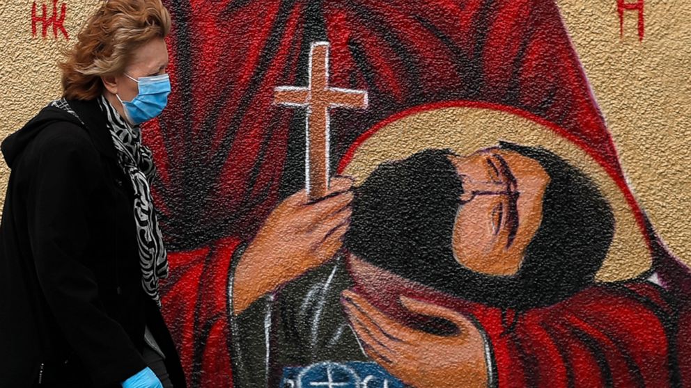 A woman wearing a protective face mask passes by graffiti depicting a Christian Orthodox icon in Belgrade, Serbia, Wednesday, May 27, 2020. (AP Photo/Darko Vojinovic)