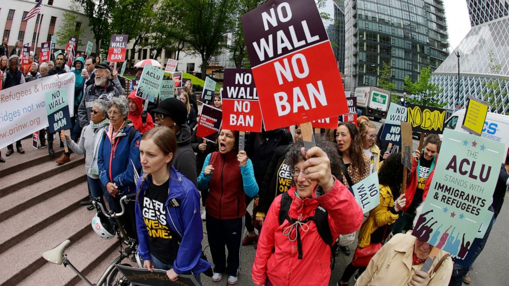 FILE - In this May 15, 2017 file photo, protesters wave signs and chant during a demonstration against President Donald Trump's revised travel ban outside a federal courthouse in Seattle. The Trump administration has agreed to speed up the cases of s