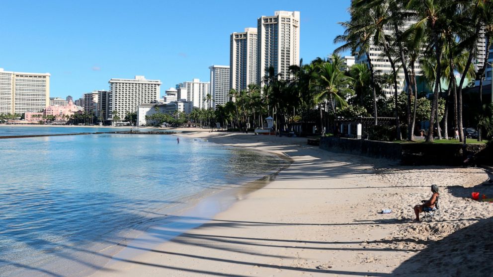 A man sits on a nearly empty Waikiki Beach in Honolulu, Friday, Oct. 2, 2020. After a summer marked by a surge of coronavirus cases in Hawaii, officials plan to reboot the tourism based economy later this month despite concerns about the state's pre-