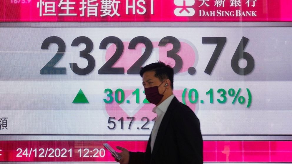 A man walks past a bank's electronic board showing the Hong Kong share index at Hong Kong Stock Exchange Friday, Dec. 24, 2021. Asian stock markets rose Friday after Wall Street hit a new high as fears of the coronavirus's omicron variant eased. Toky
