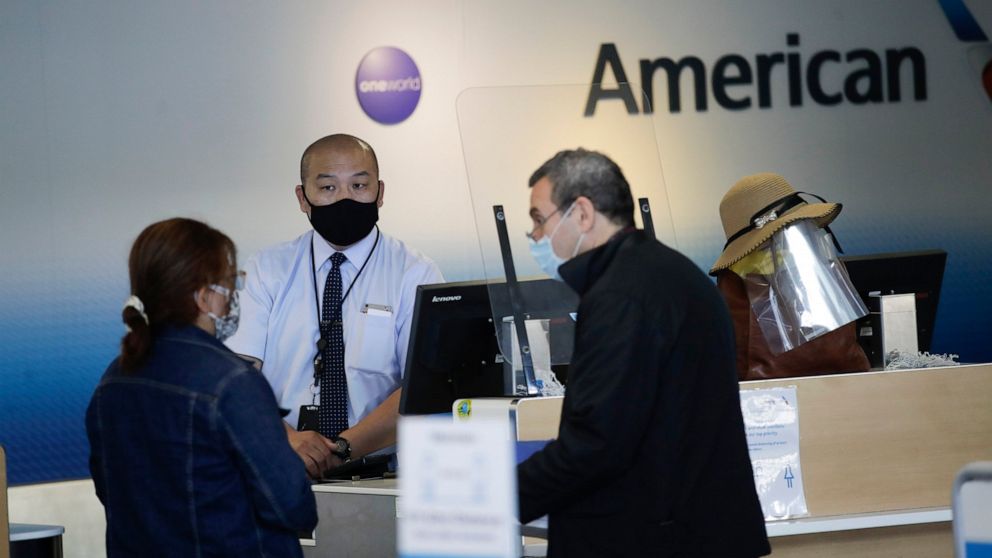 FILE - In this May 28, 2020 file photo, travelers check in at the American Airlines terminal at the Los Angeles International Airport in Los Angeles. American Airlines says it will furlough or lay off 19,000 employees in October as it struggles with 
