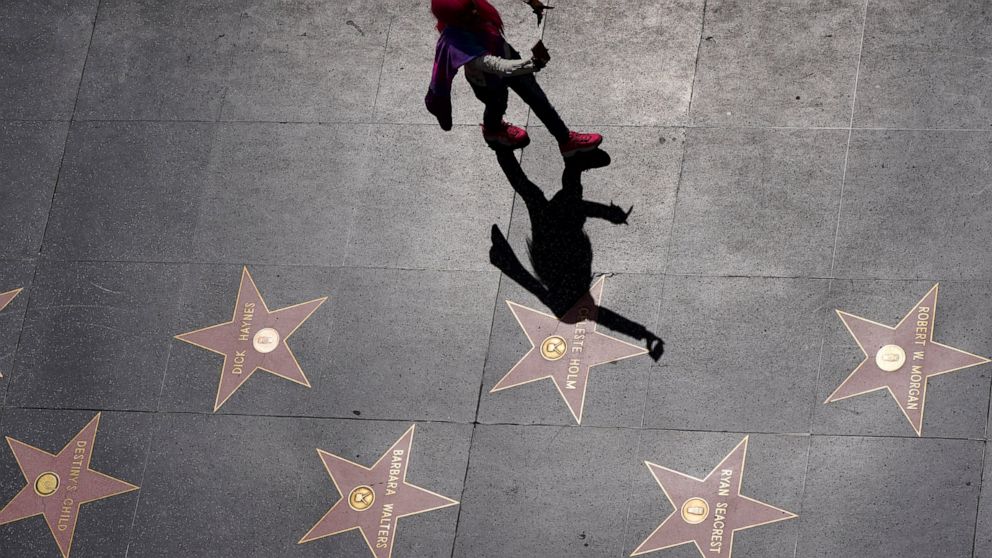 In this photo taken Wednesday, March 18, 2020, a person takes a selfie as she walks along the Walk of Fame on Hollywood Boulevard in the Hollywood section of Los Angeles. The coronavirus is hitting California's most famous tourist sites hard. From Di
