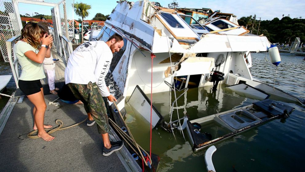 A couple look at a damaged boat in a marina at Tutukaka, New Zealand, Sunday, Jan. 16, 2022, after waves from a volcano eruption swept into the marina. An undersea volcano erupted in spectacular fashion Saturday near the Pacific nation of Tonga, send