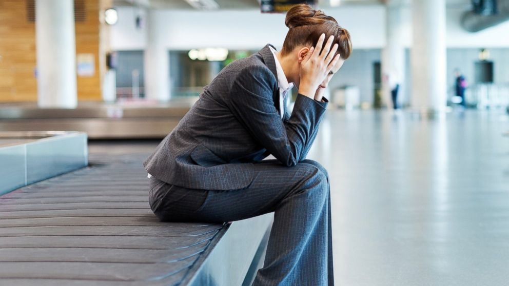 A woman holds her head while sitting on a baggage claim carousel in an undated stock photo.