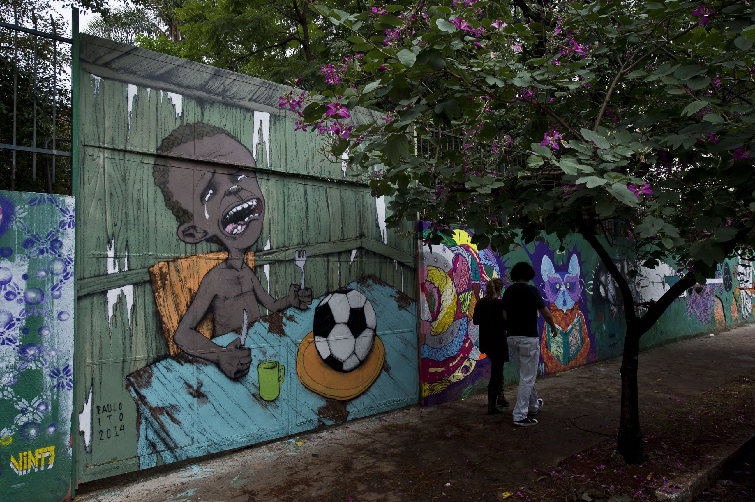 PHOTO: People walk past a graffiti painted by Brazilian street artist Paulo Ito on the entrance of a public schoolhouse in Sao Paulo, Brazil on May 23, 2014.