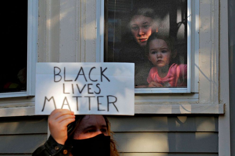 PHOTO: A woman and child watch from a window as demonstrators pass by protesting against racial inequality in the aftermath of the death of George Floyd, in Salem, Mass., June 12, 2020.