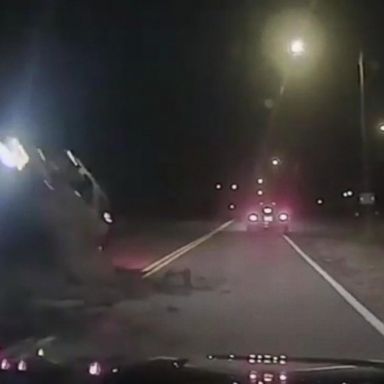 VIDEO: A car hits fallen rocks on a roadway and flips into a police cruiser at the scene, trapping the officer inside.