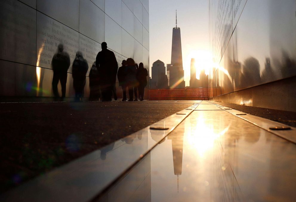 PHOTO: The sun rises behind the skyline of lower Manhattan and One World Trade Center in New York City as people walk through the Empty Sky 9/11 Memorial as seen from Jersey City, N.J., April 24, 2021.