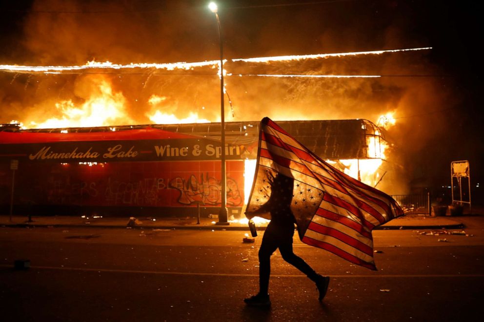 PHOTO: A protester carries the carries a U.S. flag upside, a sign of distress, next to a burning building Thursday, May 28, 2020, in Minneapolis. Protests over the death of George Floyd, a black man who died in police custody Monday.
