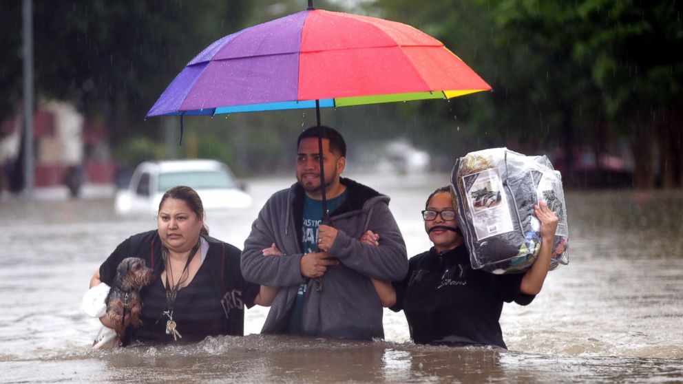 PHOTO: Felix Yanez, center, helps Lucy Olvio, right, and Judy wade through floodwaters as they evacuate from their flooded apartment complex, April 18, 2016, in Houston. 