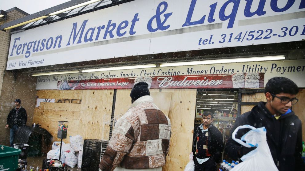 FILE - In this Wednesday, Nov. 26, 2014, file photo, Kush Patel, right, carries out bags of merchandise while helping his uncle Andy Patel, rear, clean up the looting damage from Monday's riots at his store, Ferguson Market and Liquor, in Ferguson, Mo. 