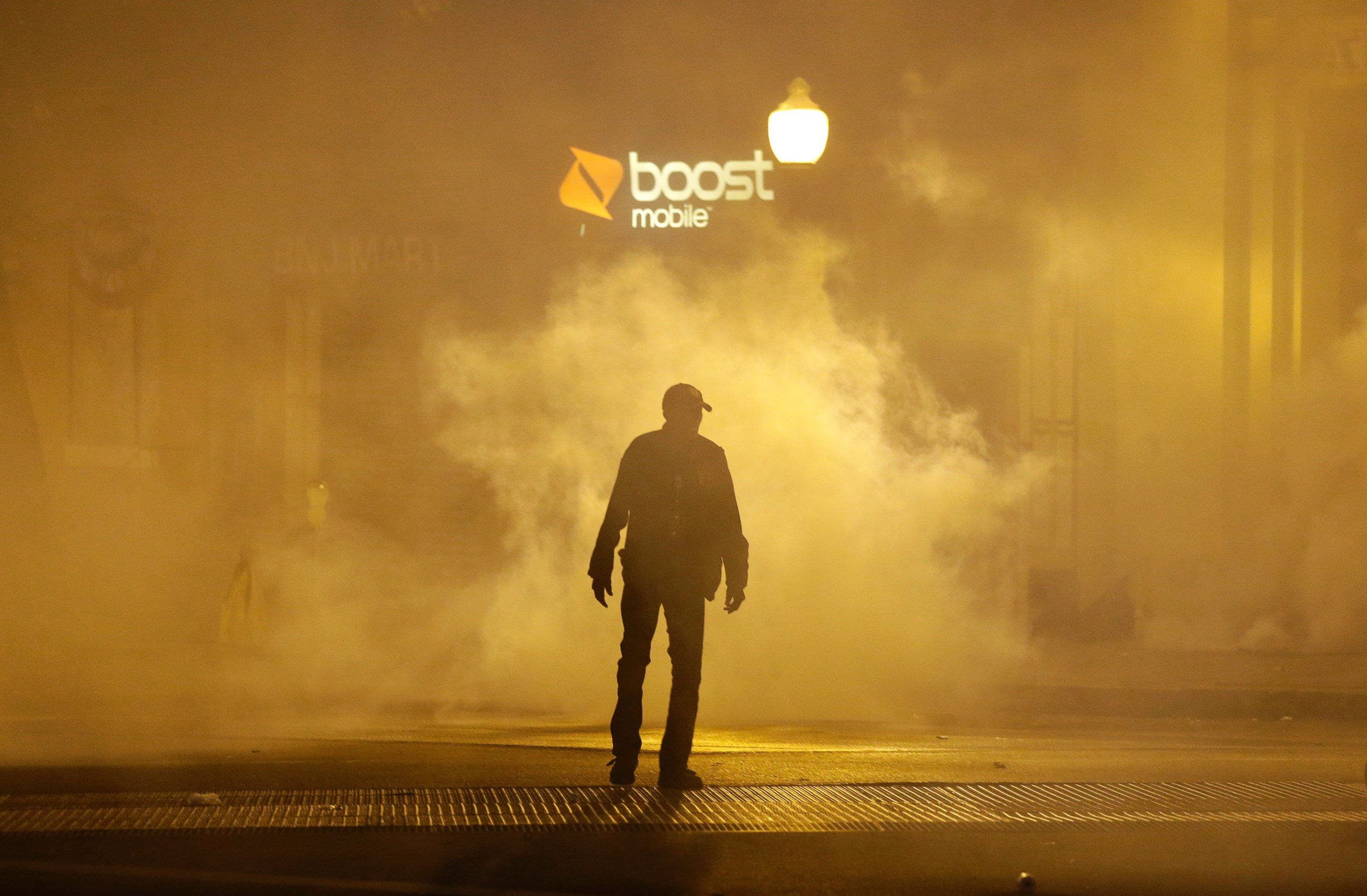 A man walks through a cloud of tear gas as police enforce curfew, Tuesday, April 28, 2015, in Baltimore, a day after unrest that occurred following Freddie Gray's funeral.