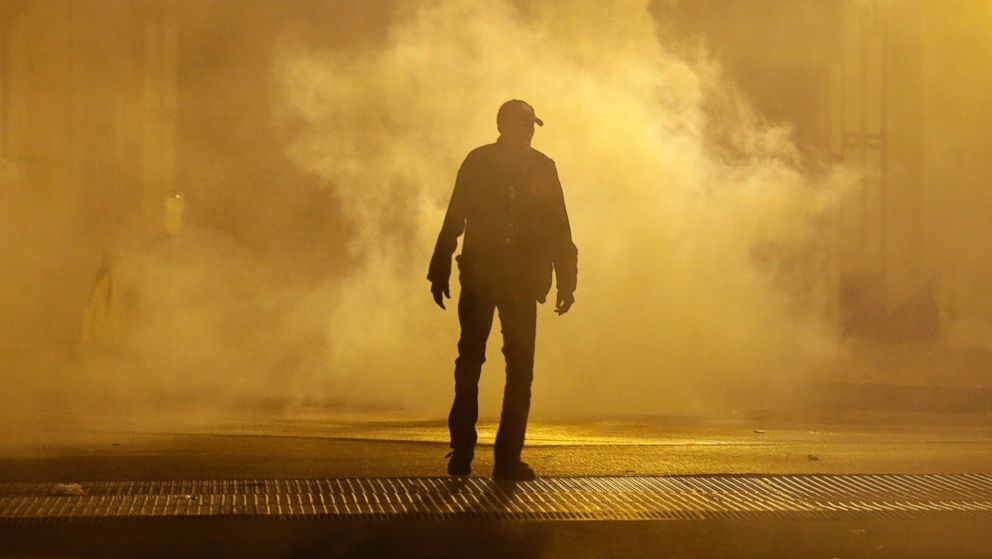 A man walks through a cloud of tear gas as police enforce curfew, Tuesday, April 28, 2015, in Baltimore, a day after unrest that occurred following Freddie Gray's funeral.