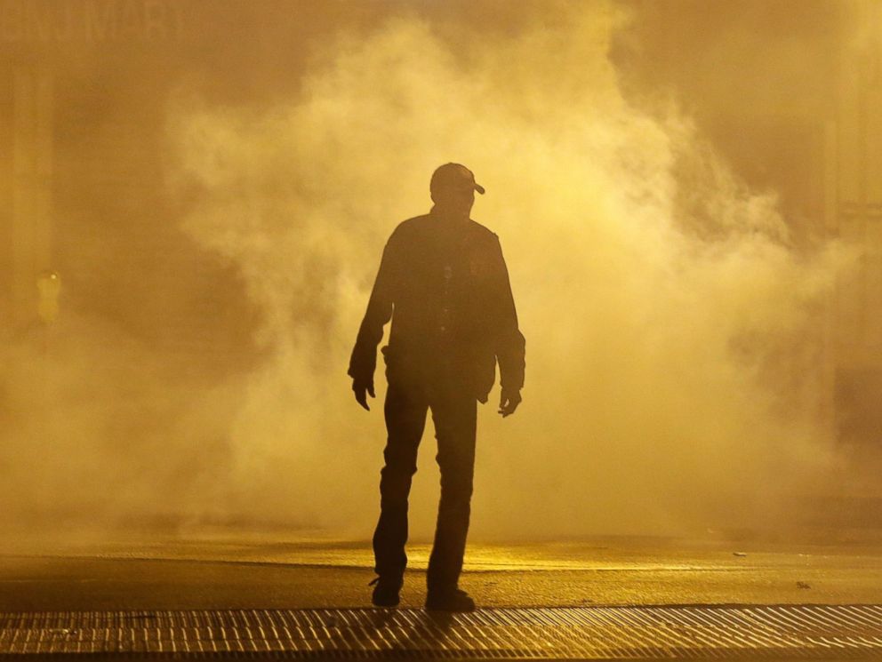A man walks through a cloud of tear gas as police enforce curfew, Tuesday, April 28, 2015, in Baltimore, a day after unrest that occurred following Freddie Grays funeral.