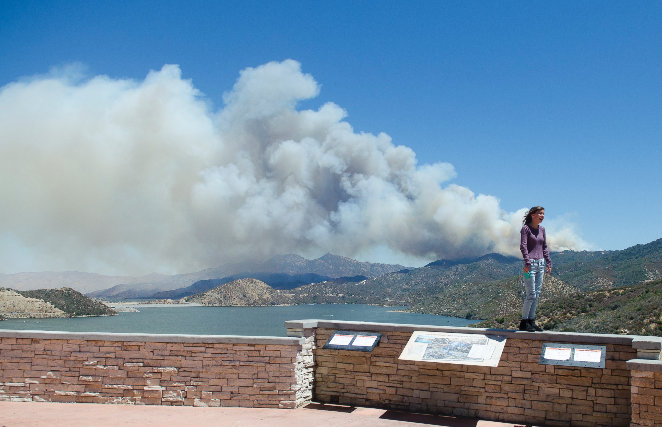 PHOTO: A wildfire burns in the background behind a sightseer as smoke billows over Silverwood Lake on Aug. 7, 2016, in Crestline, California.