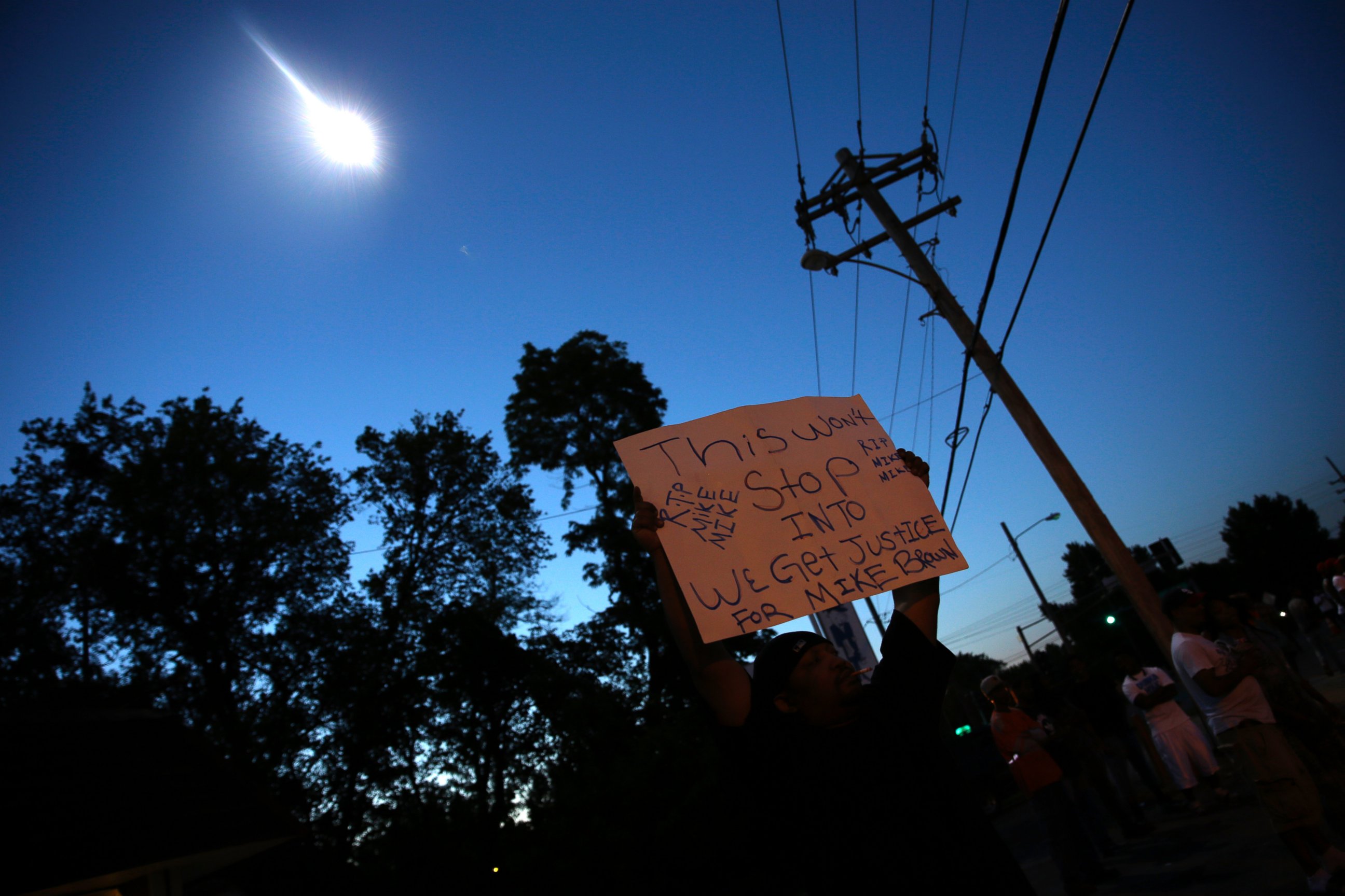 PHOTO: A protester holds up a sign as a police helicopter circles overhead, Aug. 13, 2014, in Ferguson, Mo.