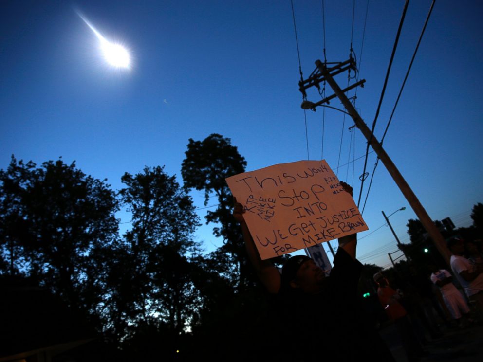 PHOTO: A protester holds up a sign as a police helicopter circles overhead, Aug. 13, 2014, in Ferguson, Mo.