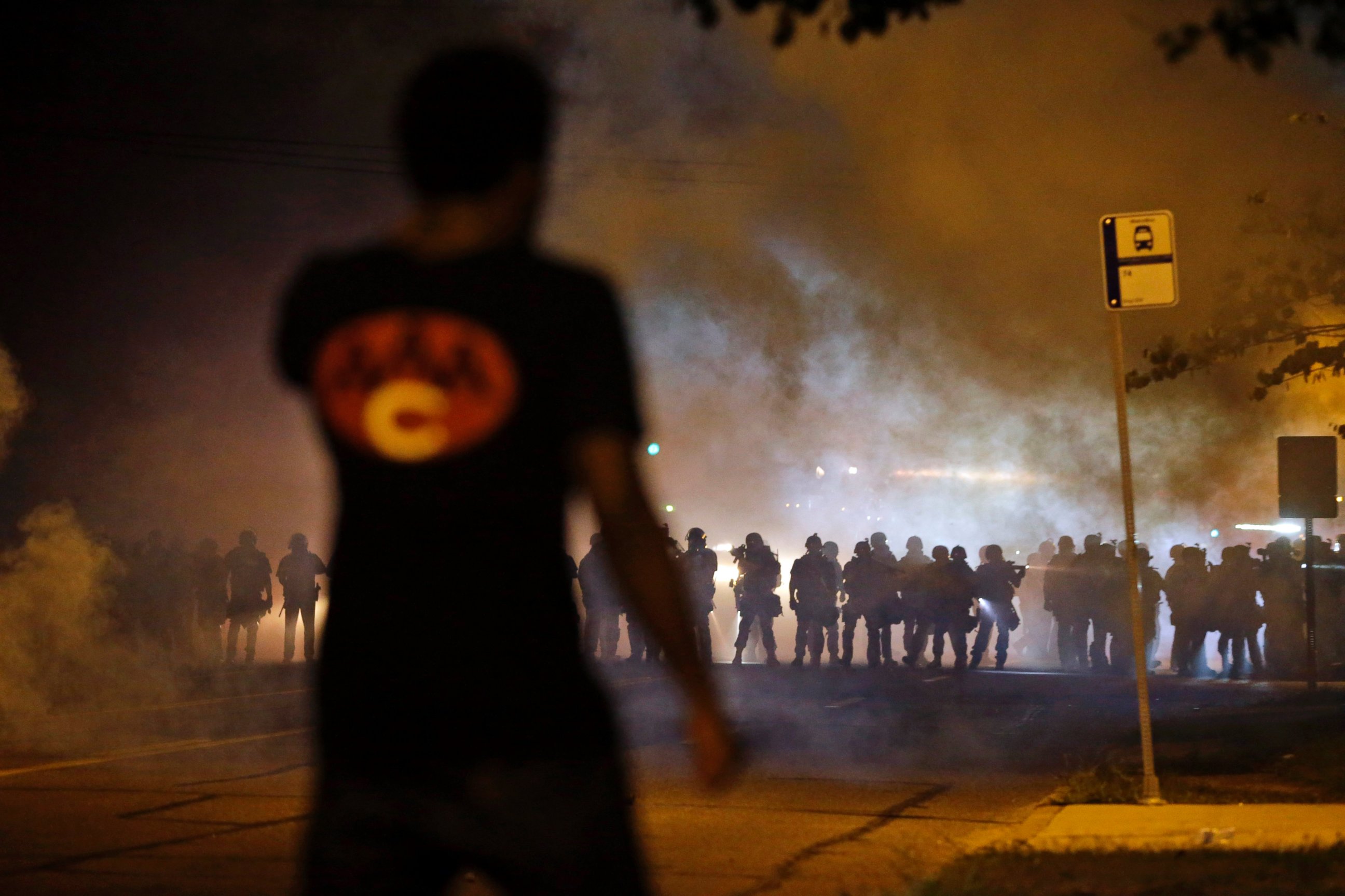 PHOTO: A man watches as police walk through a cloud of smoke during a clash with protesters, Aug. 13, 2014, in Ferguson, Mo.