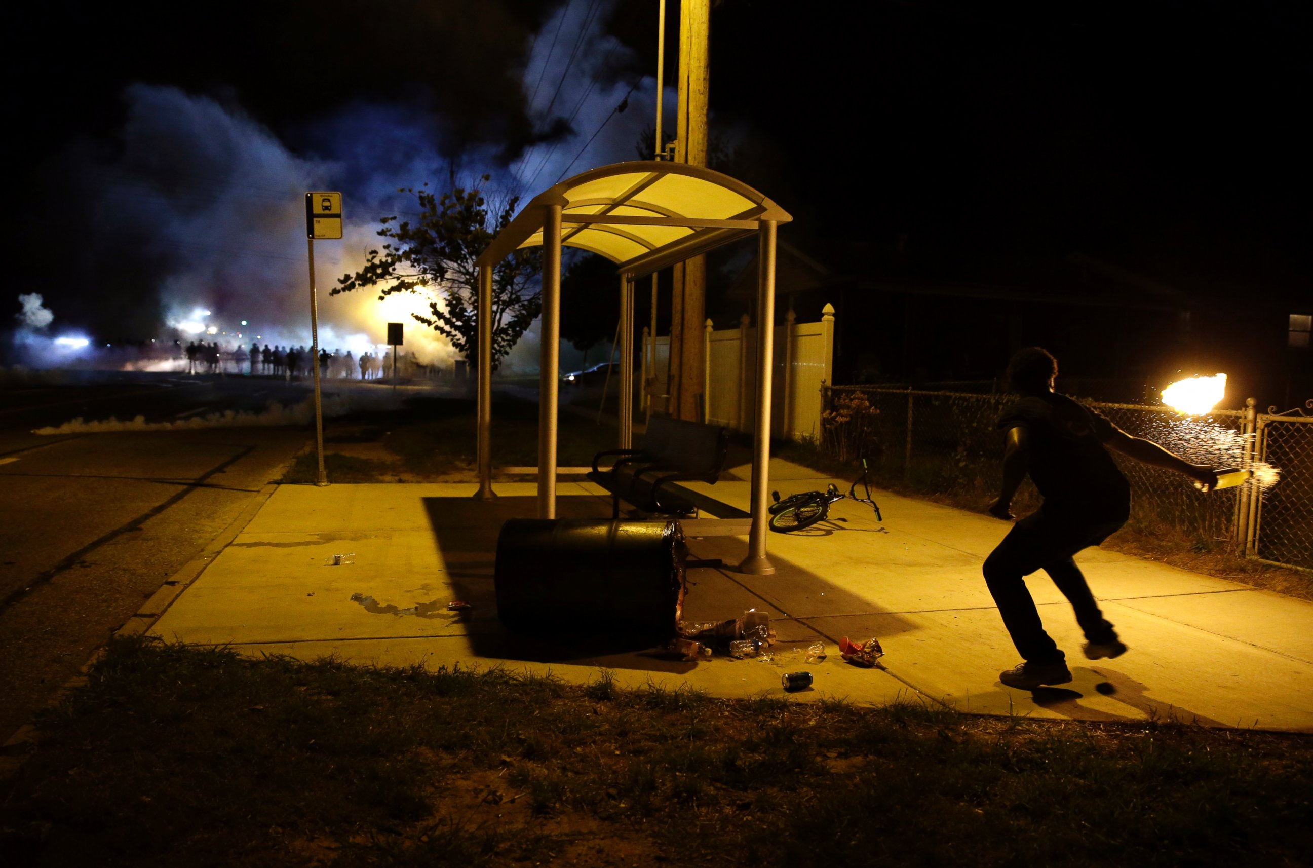 PHOTO: A man picks up a flaming bottle and prepares to throw it as a line of police advance in the distance, Aug. 13, 2014, in Ferguson, Mo.