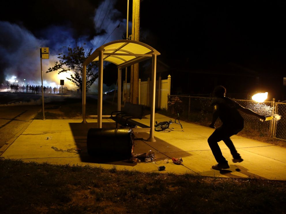 PHOTO: A man picks up a flaming bottle and prepares to throw it as a line of police advance in the distance, Aug. 13, 2014, in Ferguson, Mo.