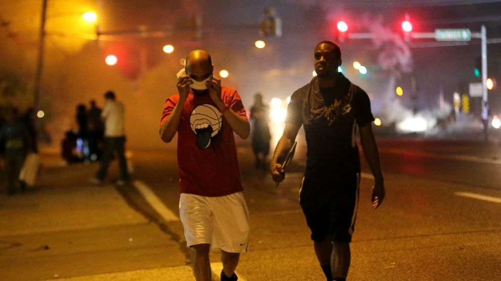 Men walk away from a cloud of tear gas during a protest, Aug. 18, 2014, in Ferguson, Mo.