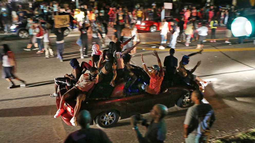People drive down the street honking their horns, raising their arms, and holding signs on in Ferguson, Mo., Aug. 14, 2014.