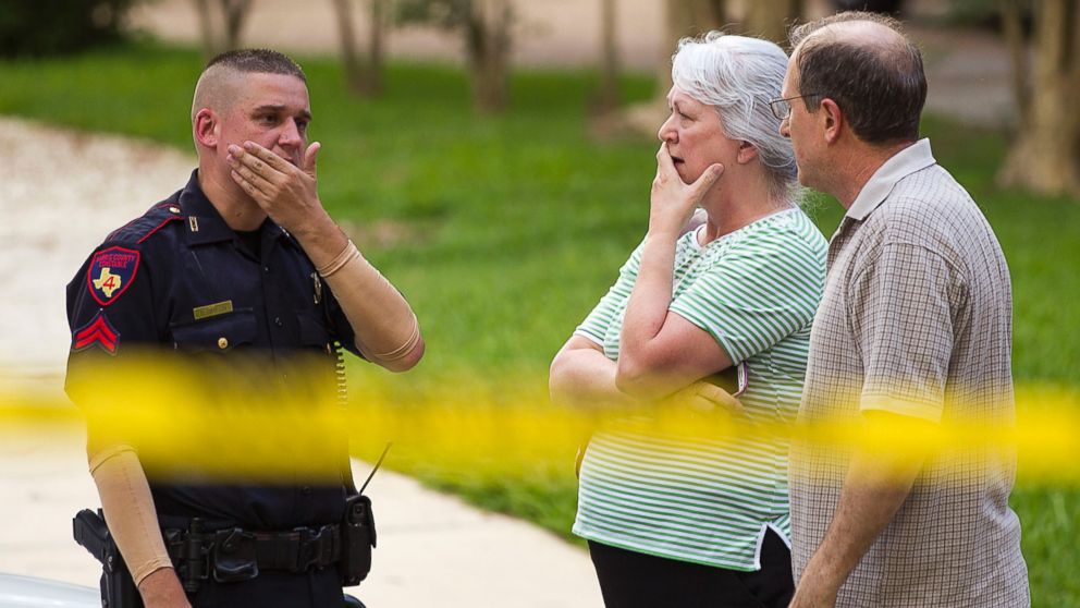 People stand with a law enforcement officer near the scene of a shooting, July 9, 2014, in Spring, Texas.