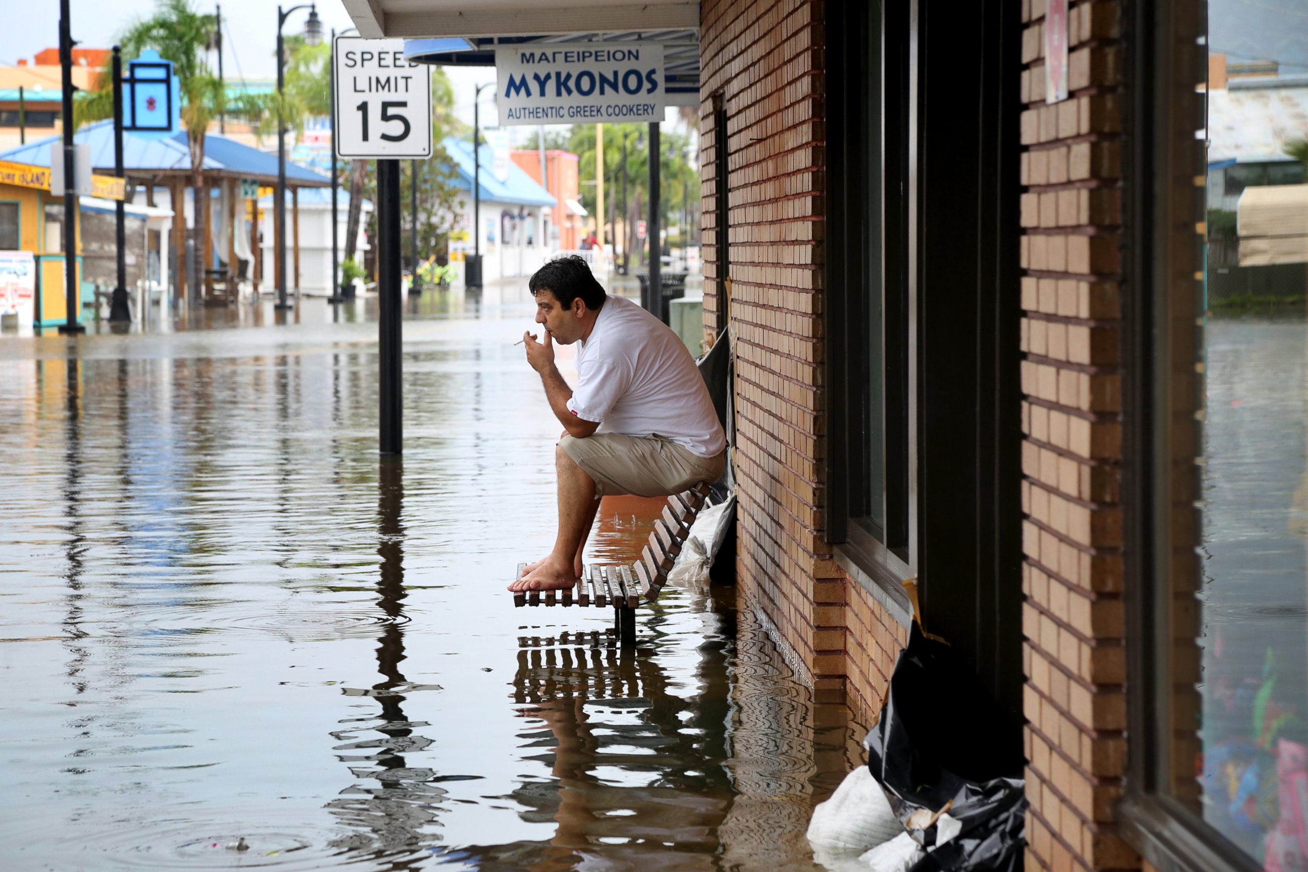 PHOTO: Pedro Muacaj rests on higher ground in front of a gift shop along a flooded section of  Dodecanese Blvd. in Tarpon Springs, Fla. where he was working, Sept. 1, 2016. 
