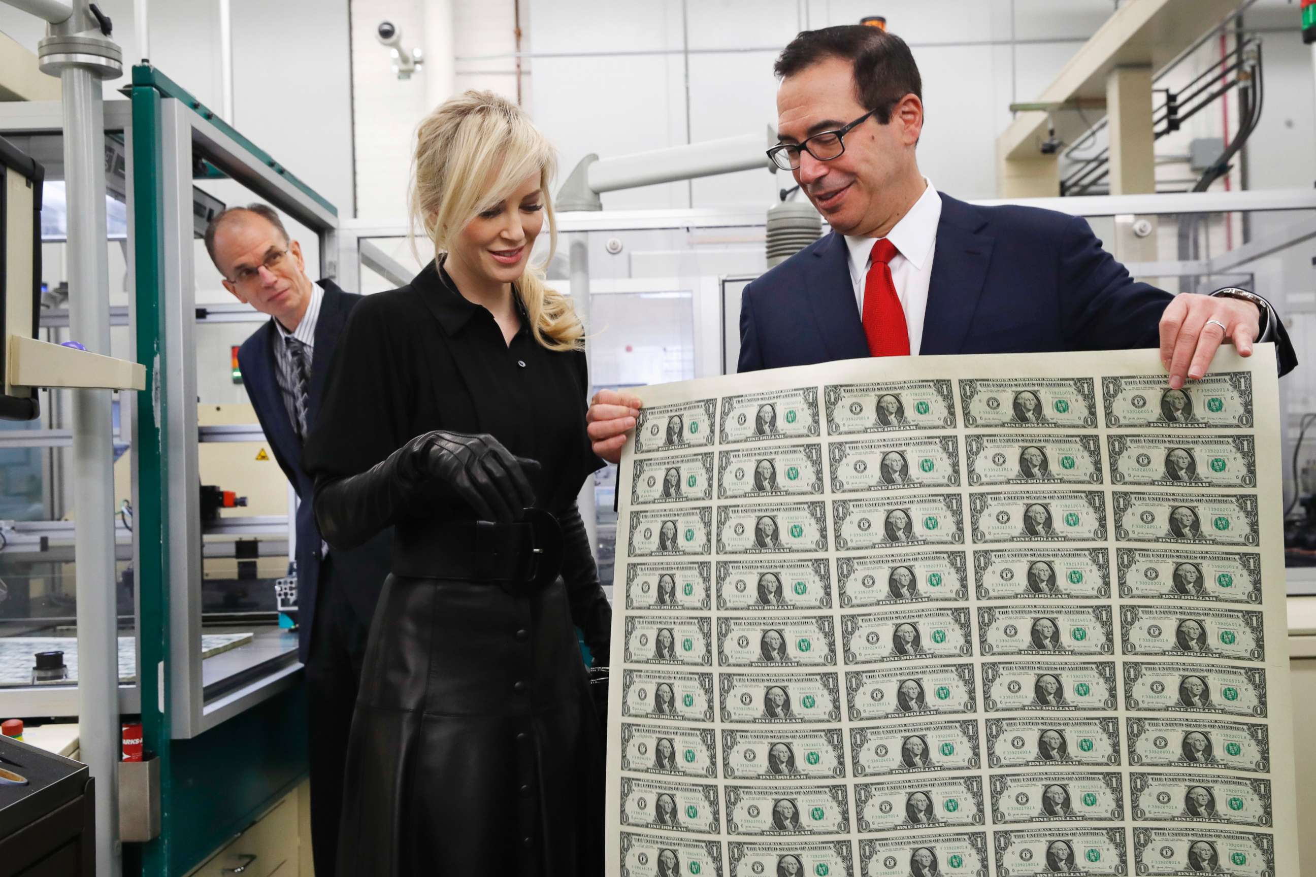 Treasury Secretary Steven Mnuchin, right, shows his wife Louise Linton a sheet of new $1 bills, the first currency notes bearing his and U.S. Treasurer Jovita Carranza's signatures, Wednesday, Nov. 15, 2017.