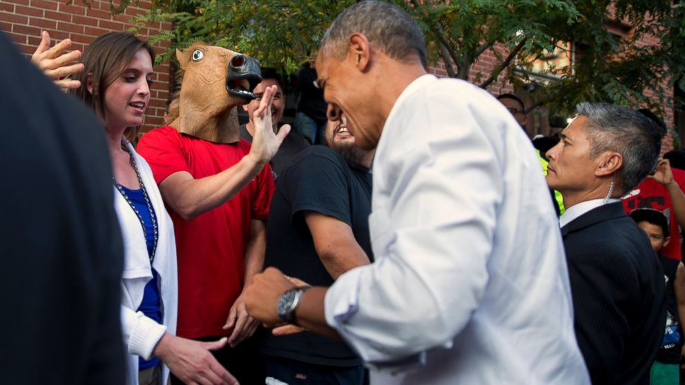 President Barack Obama laughs as he spots a man wearing a horse-head mask during an impromptu walk after having dinner at Wazee Supper Club, July 8, 2014, in Denver.
