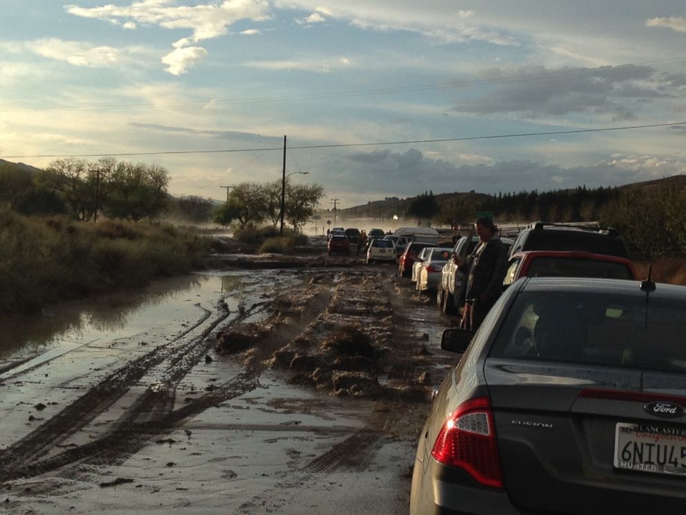 PHOTO: In a photo provided by Robert Rocha, cars on a road are stopped because of flooding, with some stuck in the mud in the distance, in Lake Hughes, Calif.