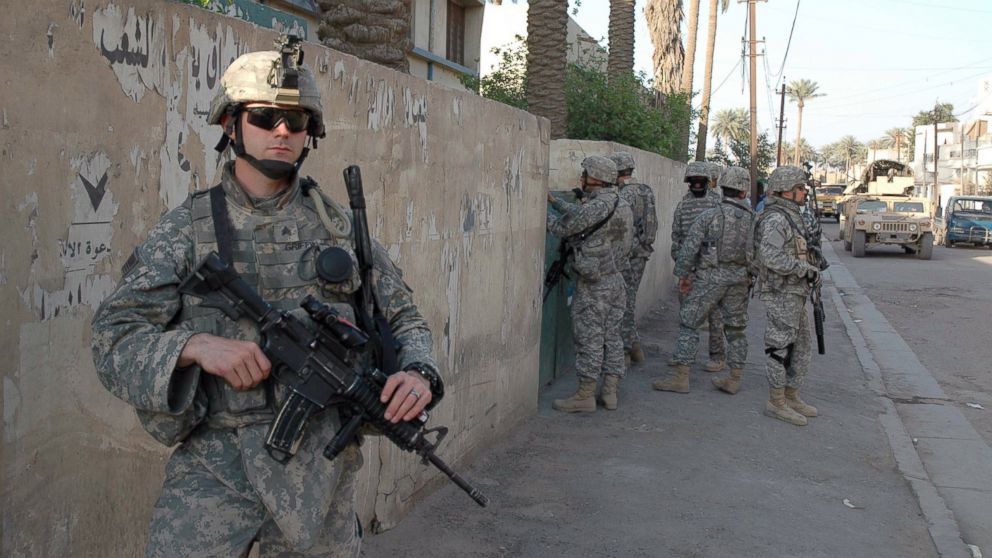 A paratrooper of the US Company D of the 1st Battalion "Red Falcons" holds his M4A1 carabine as his fellow soldiers knock on a gate during a knock and search operation in the Kadamiyah district of Bagdad, March 2007.  