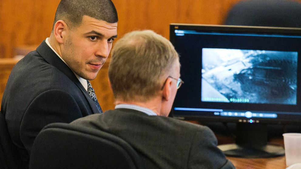 Former NFL player Aaron Hernandez looks at his attorney as security footage plays on a monitor during his murder trial at the Bristol County Superior Court in Fall River, Mass., Feb. 20, 2015. 