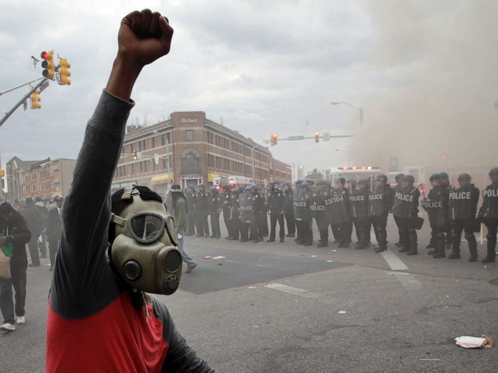 PHOTO: A demonstrator raises his fist as police stand in formation as a store burns, April 27, 2015, in Baltimore.