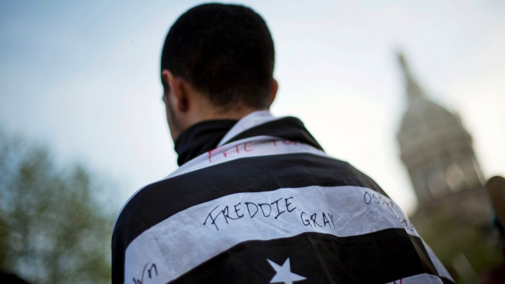 PHOTO: A protestor wears a flag decorated with the name of Freddie Gray during a demonstration outside City Hall, April 29, 2015, in Baltimore.