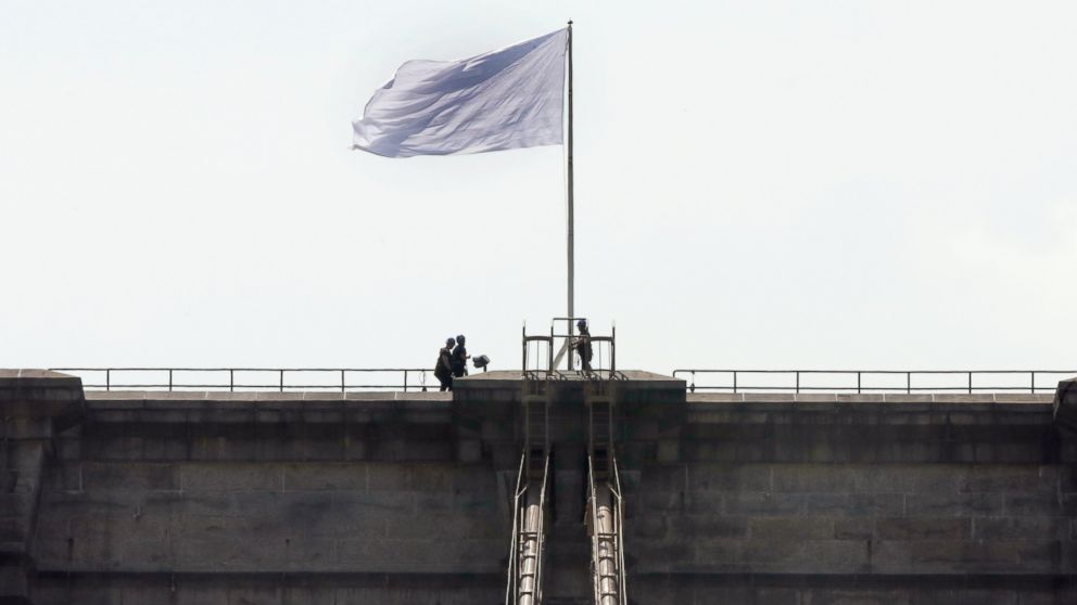New York City Police officers stand at the base of a white flag flying atop the west tower of the Brooklyn Bridge in New York City on July 22, 2014. 
