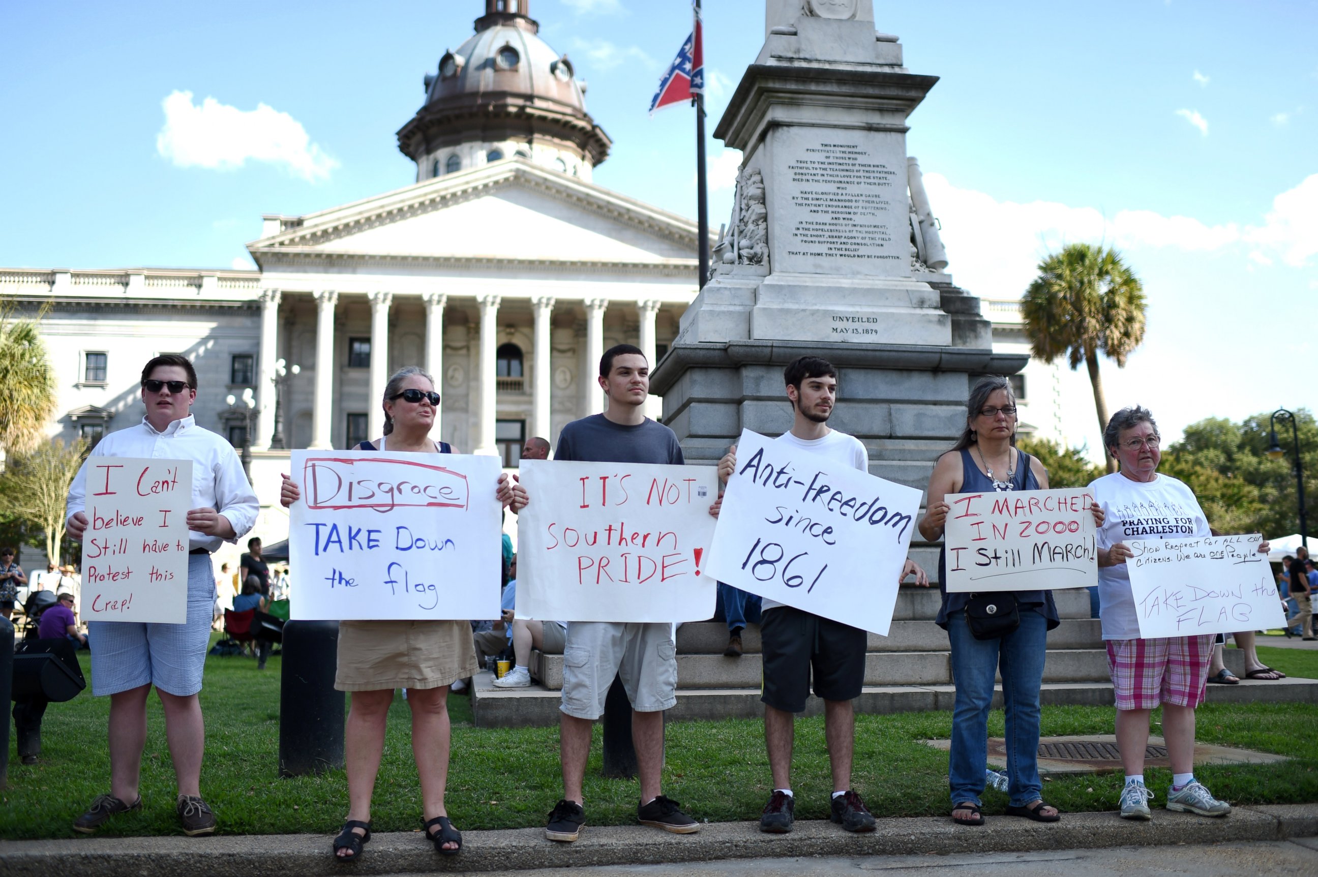 PHOTO: Protesters hold signs in front of the Confederate flag during a rally to take down the flag at the South Carolina Statehouse, June 20, 2015, in Columbia, S.C.