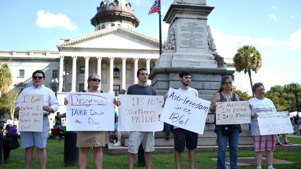 PHOTO: Protesters hold signs in front of the Confederate flag during a rally to take down the flag at the South Carolina Statehouse, June 20, 2015, in Columbia, S.C.