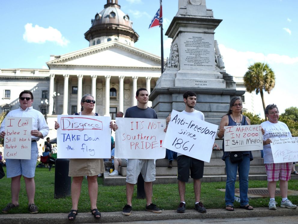 PHOTO: Protesters hold signs in front of the Confederate flag during a rally to take down the flag at the South Carolina Statehouse, June 20, 2015, in Columbia, S.C.