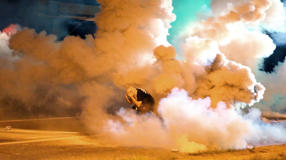 A protester takes shelter from smoke billowing around him, Aug. 13, 2014, in Ferguson, Mo.