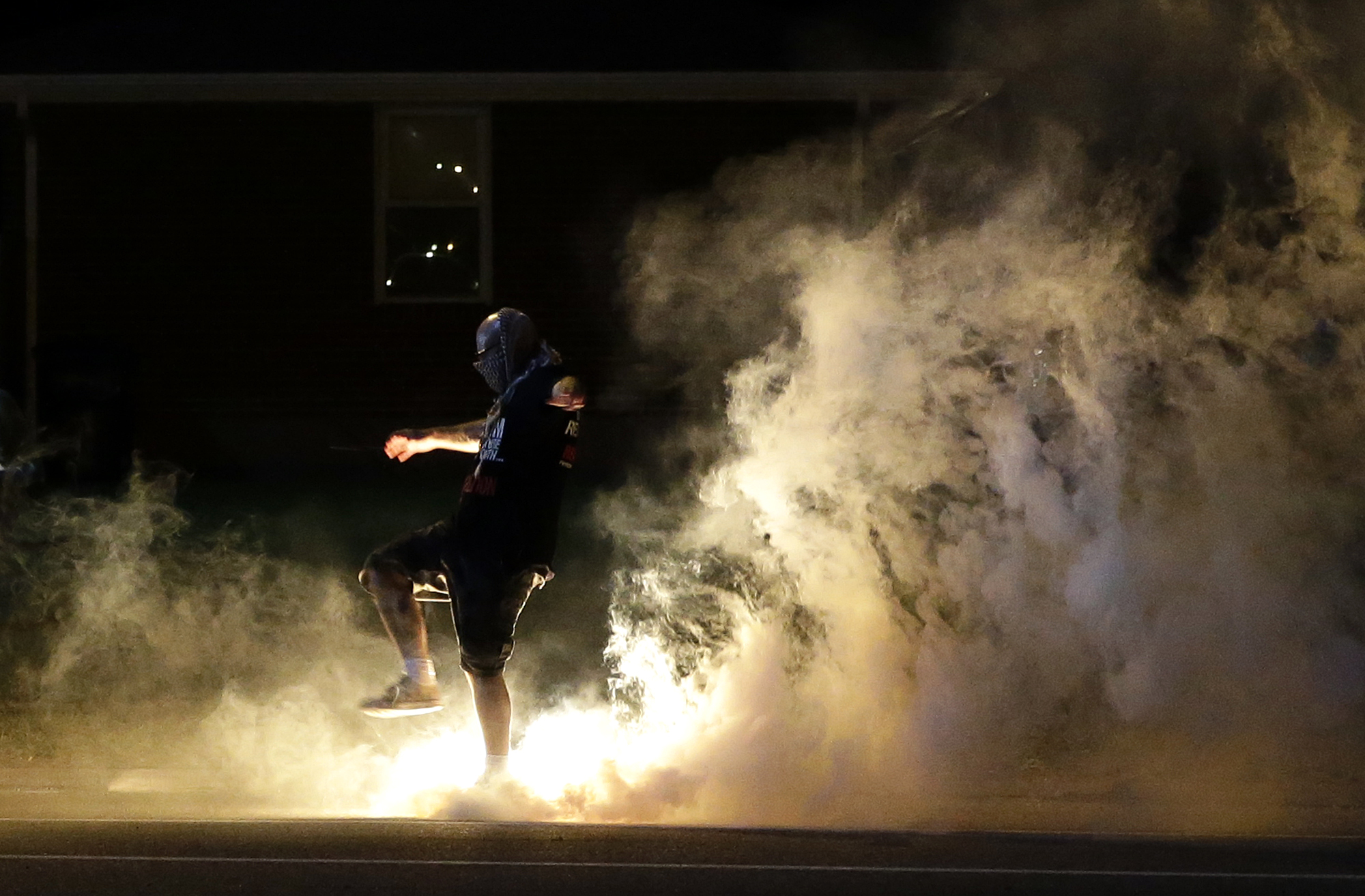 PHOTO: A protester kicks a smoke grenade that had been deployed by police back in the direction of police, Aug. 13, 2014, in Ferguson, Mo.