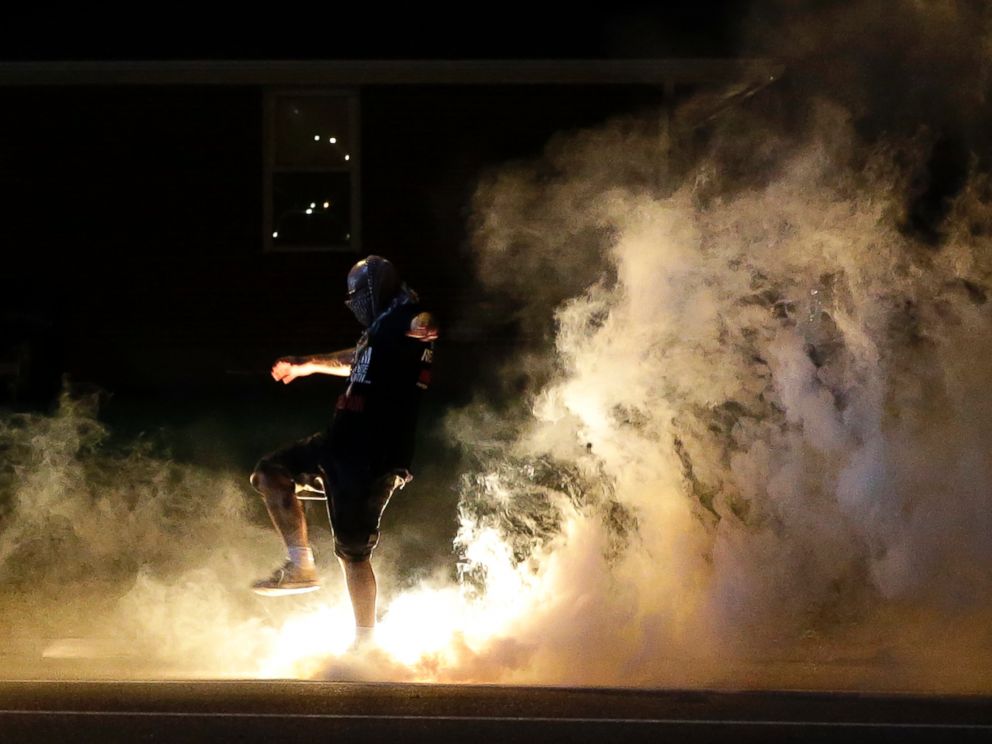 PHOTO: A protester kicks a smoke grenade that had been deployed by police back in the direction of police, Aug. 13, 2014, in Ferguson, Mo.