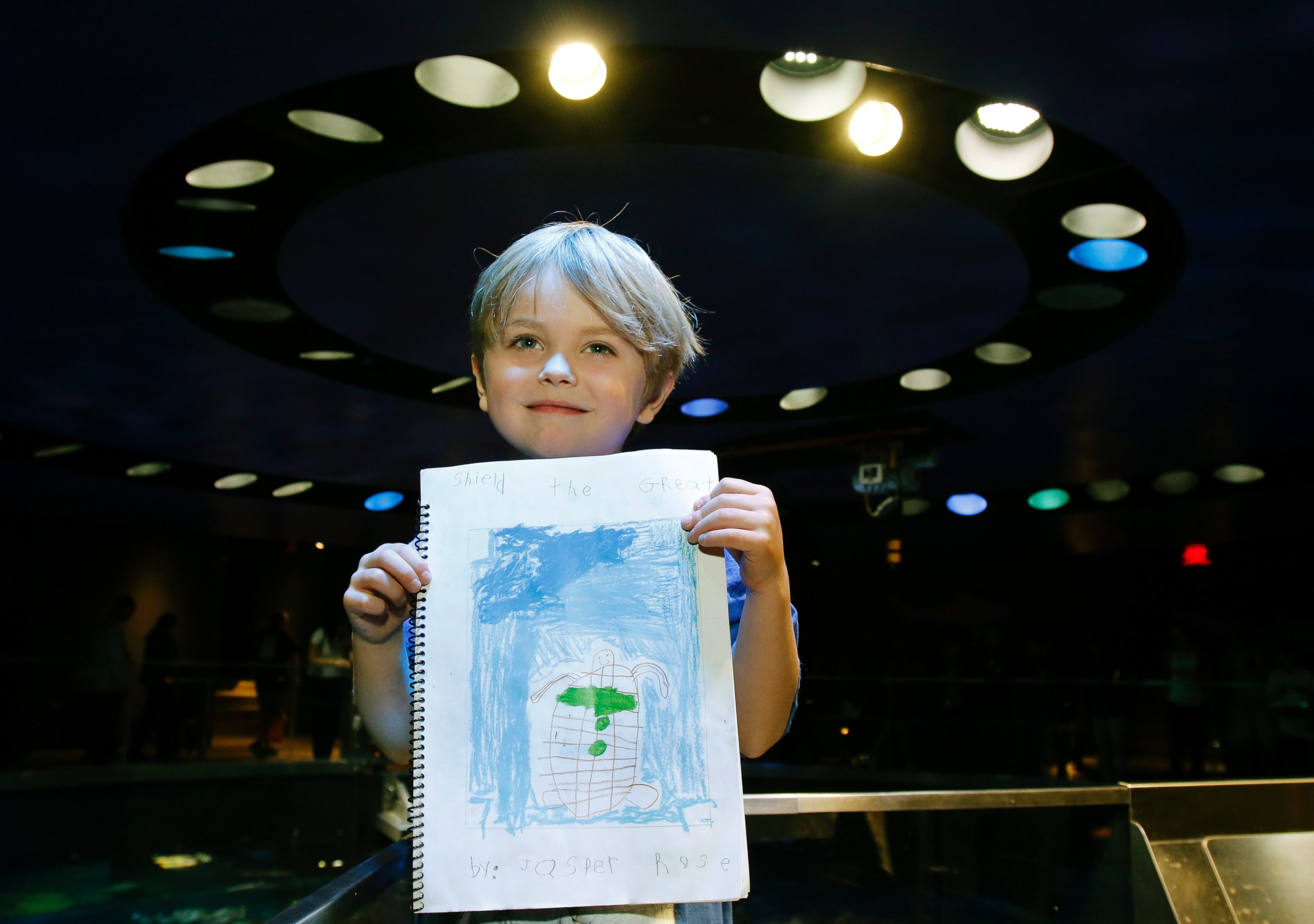 PHOTO: Jasper Rose, of Watertown, Mass., holds a booklet he created about turtles as he stands by the main tank at the New England Aquarium, April 22, 2016, in Boston.
