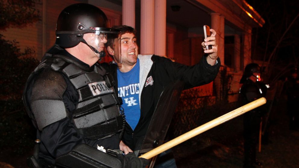 PHOTO: Eastern Kentucky University junior Eric Kuertz, right, takes a selfie with UK Police officer Lt. Greg Hall as Kentucky fans react to their teams semi-final victory on State St., Saturday, April 5, 2014, in Lexington, Ky.