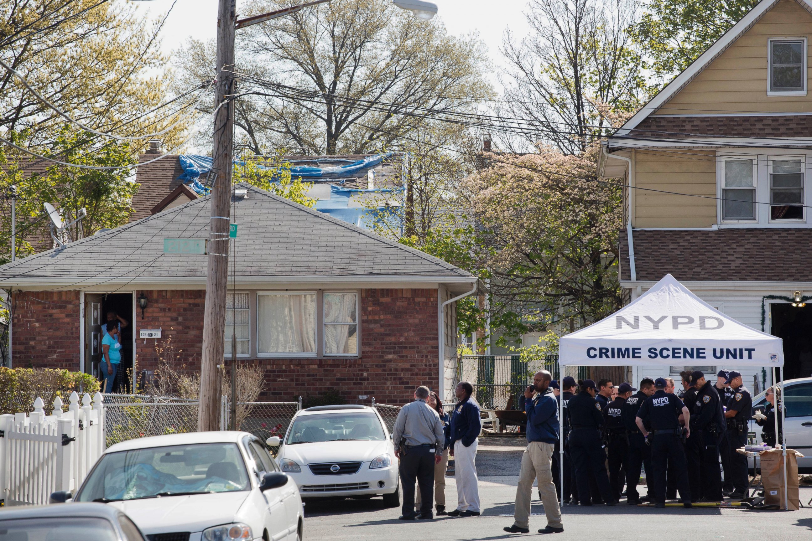 PHOTO: Residents stand in the doorway of their home, left, as they watch police officers investigate the scene of a shooting in the Queens borough of New York, Sunday, May 3, 2015. 