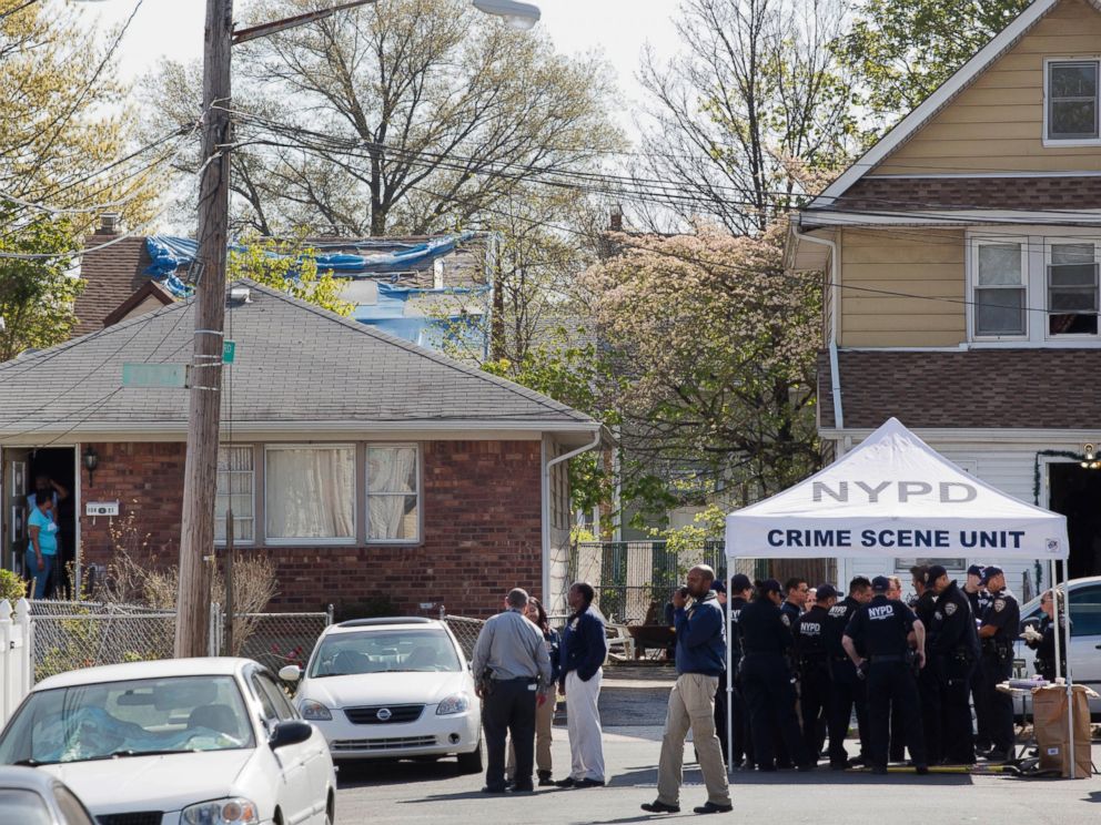 PHOTO: Residents stand in the doorway of their home, left, as they watch police officers investigate the scene of a shooting in the Queens borough of New York, Sunday, May 3, 2015.