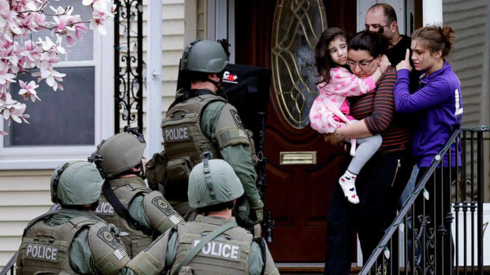 PHOTO: A woman carries a girl from their home as a SWAT team searching for a suspect in the Boston Marathon bombings enters the building in Watertown, Mass., April 19, 2013.