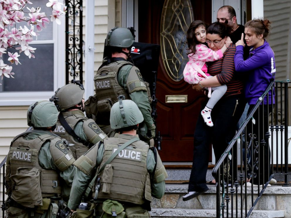 PHOTO: A woman carries a girl from their home as a SWAT team searching for a suspect in the Boston Marathon bombings enters the building in Watertown, Mass., April 19, 2013.